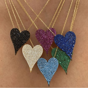 Może przedstawiać: Pięć złotych naszyjników z serduszkami. Serduszka są pokryte małymi, kolorowymi kamieniami. Kolory kamieni to czarny, biały, różowy, niebieski i zielony.