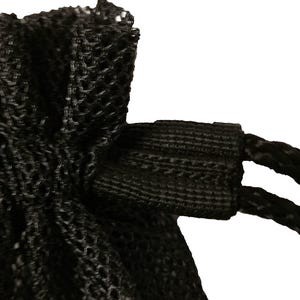 Può includere: Primo piano di un sacco a rete nero con chiusura a coulisse. Il materiale della borsa ha un motivo intrecciato e aperto. Il cordoncino è fatto di una corda nera spessa e la borsa è su uno sfondo bianco.
