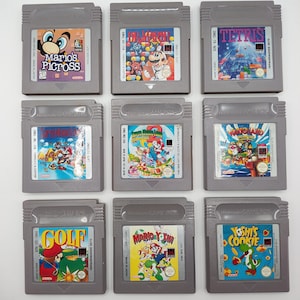 May include: Nine gray Nintendo Game Boy cartridges featuring various game titles. Titles include "Mario's Picross", "Dr. Mario", "Tetris", "Super Mario Land", "Golf", "Mario & Yoshi", and "Yoshi's Cookie". Each cartridge has colorful game art.