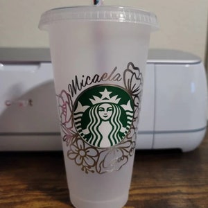 Op de afbeelding: Een doorzichtige plastic beker met een zilveren glitterontwerp met een Starbucks-logo en de naam "Michaela".