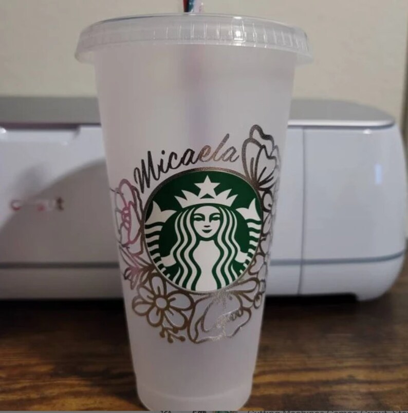 Op de afbeelding: Een doorzichtige plastic beker met een zilveren glitterontwerp met een Starbucks-logo en de naam "Michaela".