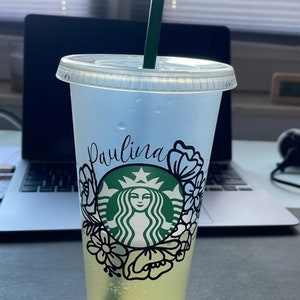 Op de afbeelding: Een doorzichtige plastic beker met een groen Starbucks-logo en een bloemenpatroon. Op de beker staat de naam "Paulina".