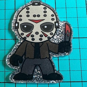 May include: A cartoon-style image of a character wearing a hockey mask, brown jacket, and gray pants, holding a bloody knife. The image has a glittery silver border and is set against a blue grid background.