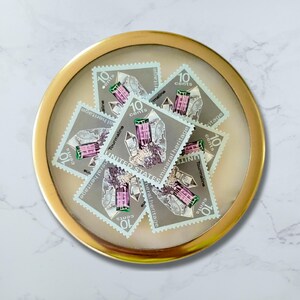 Puede incluir: Un marco circular con borde dorado contiene una colección de sellos postales estadounidenses antiguos que representan un cristal de turmalina morado y verde. Los sellos son todos de 10 centavos y tienen el texto "Mineral Heritage".