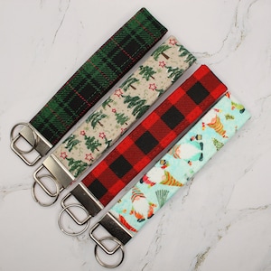 May include: Four different patterned keychains with silver key rings. The patterns include plaid, Christmas trees, gnomes, and buffalo plaid.
