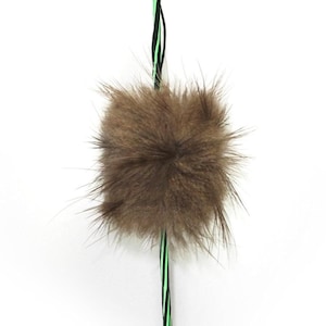May include: A brown fur pom pom attached to a green and black striped cord.