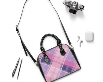 May include: A pink, purple, and white plaid pattern handbag with a black handle and strap. The bag is square-shaped with rounded edges. A camera, earbuds, and a pencil are also in the image.