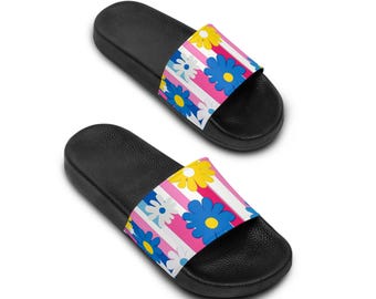 May include: A pair of black slide sandals with a colorful floral print. The print features pink, blue, yellow, and white flowers on a striped background.