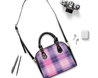 May include: A dome-shaped handbag with a pink and purple plaid pattern. The bag has black handles and a black shoulder strap. A vintage camera, wireless earbuds, and a pen and pencil are also in the image.