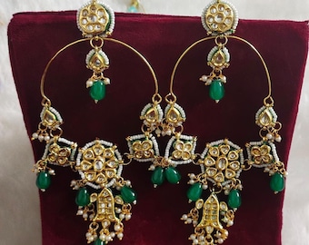 May include: A pair of gold hoop earrings with green and white beads and intricate floral designs. The earrings have a dangling section with multiple layers of beads and a large, ornate centerpiece.