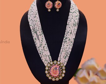 May include: A long white and green beaded necklace with a large round pendant featuring a floral design in pink, blue, and gold. The pendant is surrounded by clear stones. The necklace comes with matching earrings.