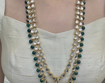 May include: A two-strand gold necklace with teardrop-shaped pendants and green beads. The necklace is made of metal and has a traditional Indian design.