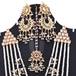 May include: A gold and white pearl necklace set with matching earrings and a maang tikka. The necklace has multiple strands of pearls and the earrings and maang tikka are decorated with gold and white stones.