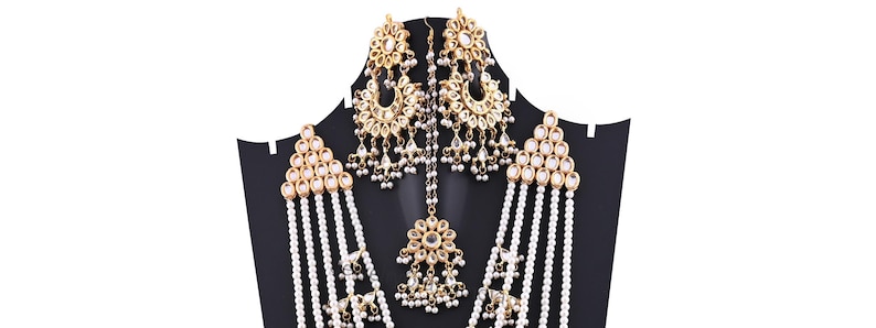 May include: A gold and white pearl necklace set with matching earrings and a maang tikka. The necklace has multiple strands of pearls and the earrings and maang tikka are decorated with gold and white stones.