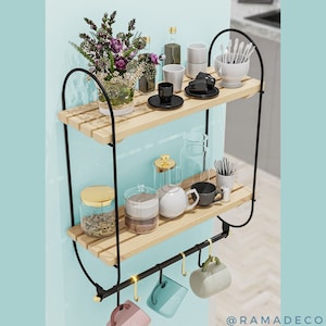Op de afbeelding: Een houten plank met twee niveaus en zwarte metalen steunen, met diverse keukenartikelen. De bovenste plank toont kopjes, schotels en een vaas met bloemen. De onderste plank heeft potten, een theepot en bekers die eronder hangen.