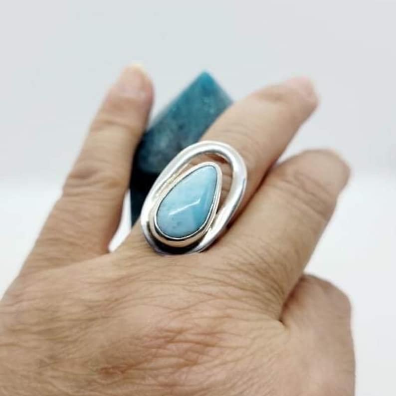 May include: A silver ring with a teardrop-shaped blue and white gemstone set in a swirling design.