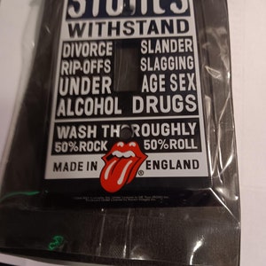 May include: A black and white light switch cover with the words "Stones Withstand" and a list of things to withstand, including "Divorce", "Slander", "Rip-offs", "Slagging", "Under", "Age Sex", "Alcohol", "Drugs", and "Wash Thoroughly". The bottom of the cover has the words "50% Rock", "50% Roll", "Made in England", and a red tongue logo.