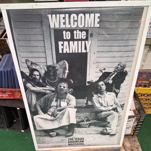 Può includere: Poster in bianco e nero del film "Non aprite quella porta". Il poster presenta il testo "WELCOME to the FAMILY" sopra un gruppo di personaggi su un portico. Una motosega è visibile sui gradini. Il titolo del film è in basso.