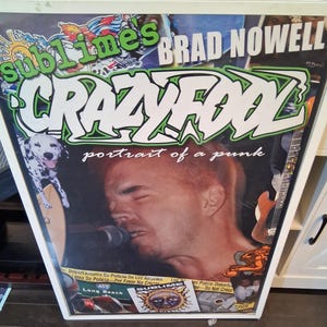 May include: Framed poster featuring Brad Nowell with the text "Crazy Fool" and "portrait of a punk." The poster includes a Dalmatian dog, a guitar, and the word "Sublimes" in green. The poster is in a white frame.
