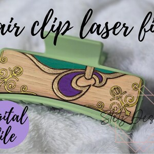 Puede incluir: Una pinza para el pelo verde con un diseño de madera que presenta un patrón de espiral morado y dorado. El diseño incluye espirales dorados y una forma de media luna morada. El texto "Stutz Designs" es visible en la esquina inferior derecha de la imagen.