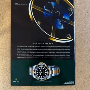 Puede incluir: Anuncio de un reloj Rolex Oyster Perpetual GMT-Master II. El reloj tiene una esfera negra, una correa de oro y plata y un bisel giratorio. El anuncio incluye texto en inglés y alemán, con una imagen detallada del reloj y un diagrama de sus componentes internos.