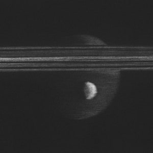 Peut inclure: Une photographie en noir et blanc des anneaux de Saturne avec les lunes Encelade et Titan visibles. Le texte "Rings of Saturn with Enceladus and Titan" est écrit en bas de l'image.