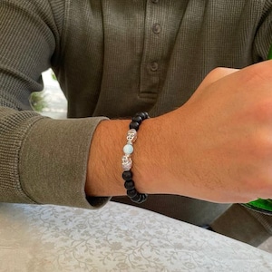 May include: A black beaded bracelet with silver Buddha head charms and a light blue stone bead.