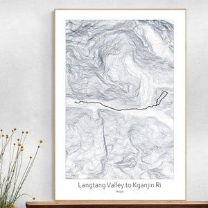 May include: A framed topographical map print of the Langtang Valley to Kganjin Ri in Nepal. The print features a grayscale rendering of the mountain range with a black line indicating a trail. The text "Langtang Valley to Kganjin Ri Nepal" is printed at the bottom.