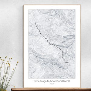 May include: Framed print featuring a topographical map of a trail. The map is in shades of gray and white, with a black line indicating the path. The text "Tikhedunga to Ghorepani Doerali Nepal" is printed at the bottom.