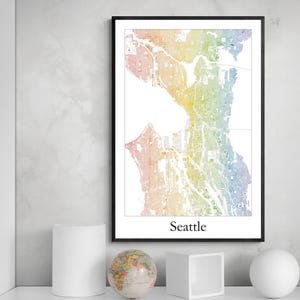 May include: A framed map of Seattle, Washington, in a rainbow colour scheme. The map is detailed, showing streets and waterways. The word "Seattle" is printed in a black font at the bottom of the frame. The frame is black.