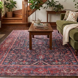 May include: A large rectangular area rug featuring a dark navy blue and deep red intricate floral pattern with a wide border, positioned in a living room under a wooden coffee table, a green velvet sofa, and a staircase with wooden railings.