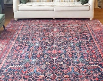 May include: A large rectangular area rug featuring a dark blue base with intricate floral and geometric patterns in shades of red, pink, and light blue. The rug is positioned in a room with a white sofa, a green armchair, and a wicker basket.
