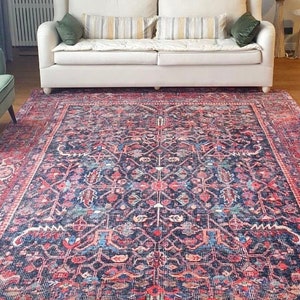 May include: A large rectangular area rug featuring a dark blue base with intricate floral and geometric patterns in shades of red, pink, and light blue. The rug is positioned in a room with a white sofa, a green armchair, and a wicker basket.