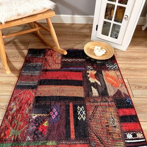 Op de afbeelding: Een kleurrijk patchwork tapijt met een rood, oranje, zwart en blauw kleurenschema. Het tapijt heeft een verscheidenheid aan geometrische patronen en ontwerpen.