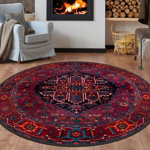 May include: A round area rug with a traditional design. The rug features a deep red background with intricate patterns in shades of blue, orange, and black. The rug is placed on a wooden floor, creating a warm and inviting atmosphere.