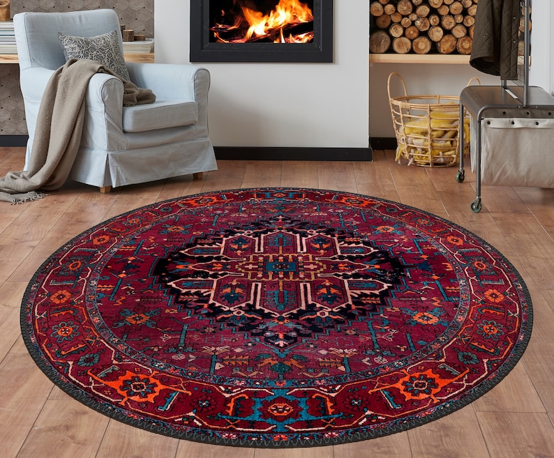 May include: A round area rug with a traditional design. The rug features a deep red background with intricate patterns in shades of blue, orange, and black. The rug is placed on a wooden floor, creating a warm and inviting atmosphere.