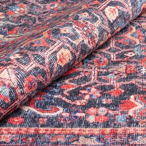 May include: A folded area rug featuring a dark navy blue background with an intricate pattern of red, cream, and light blue floral and geometric motifs. The textile displays a dense, woven texture with a visible border along the bottom edge.