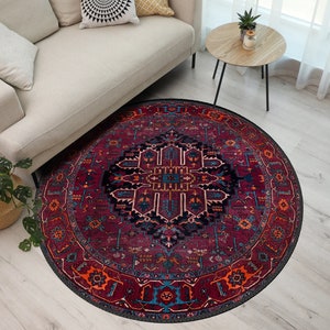 May include: A round area rug with a traditional Persian design. The rug features a deep burgundy background with intricate patterns in navy, orange, and teal. The rug is placed on a light wood floor, partially under a beige sofa.