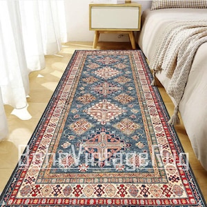 May include: A rectangular runner rug featuring a deep blue field with a repeating pattern of geometric medallions in shades of red, cream, and gold. The rug has a wide, intricate border with repeating motifs and a light-colored fringe at the ends.