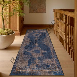Könnte beinhalten: Ein blauer und goldfarbener Läufer mit einem verwitterten Vintage-Look. Der Läufer hat ein geometrisches Muster mit einem zentralen Medaillon. Der Läufer ist perfekt, um jedem Raum einen Hauch von Eleganz zu verleihen.