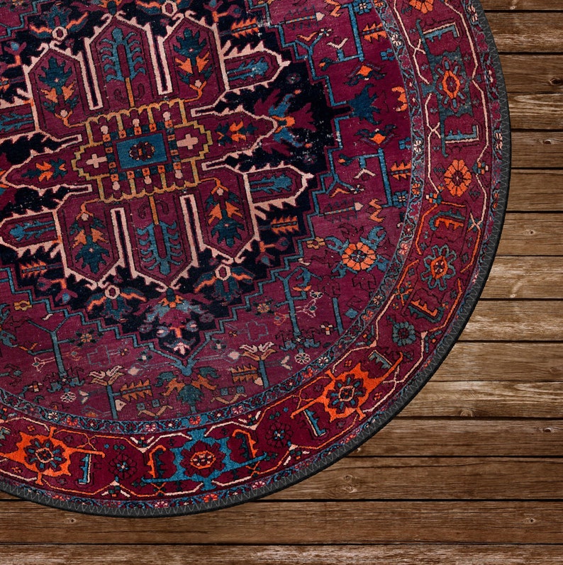 May include: A round, patterned rug with a rich burgundy background and intricate designs in teal, orange, and black. The rug's border features a detailed floral pattern. The rug is placed on a wooden floor.
