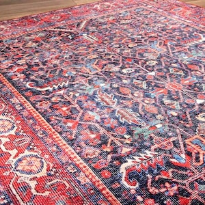 May include: A rectangular area rug featuring a dark navy blue background with an intricate pattern of red, light blue, and cream floral and geometric motifs. The rug has a wide, decorative border in vibrant red with repeating ornate patterns.