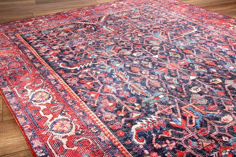 May include: A rectangular area rug featuring a dark navy blue background with an intricate pattern of red, light blue, and cream floral and geometric motifs. The rug has a wide, decorative border in vibrant red with repeating ornate patterns.