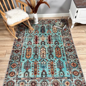 May include: A teal blue rug with a traditional Persian design. The rug features intricate patterns in shades of red, orange, yellow, and brown. The rug is laid out on a wooden floor.