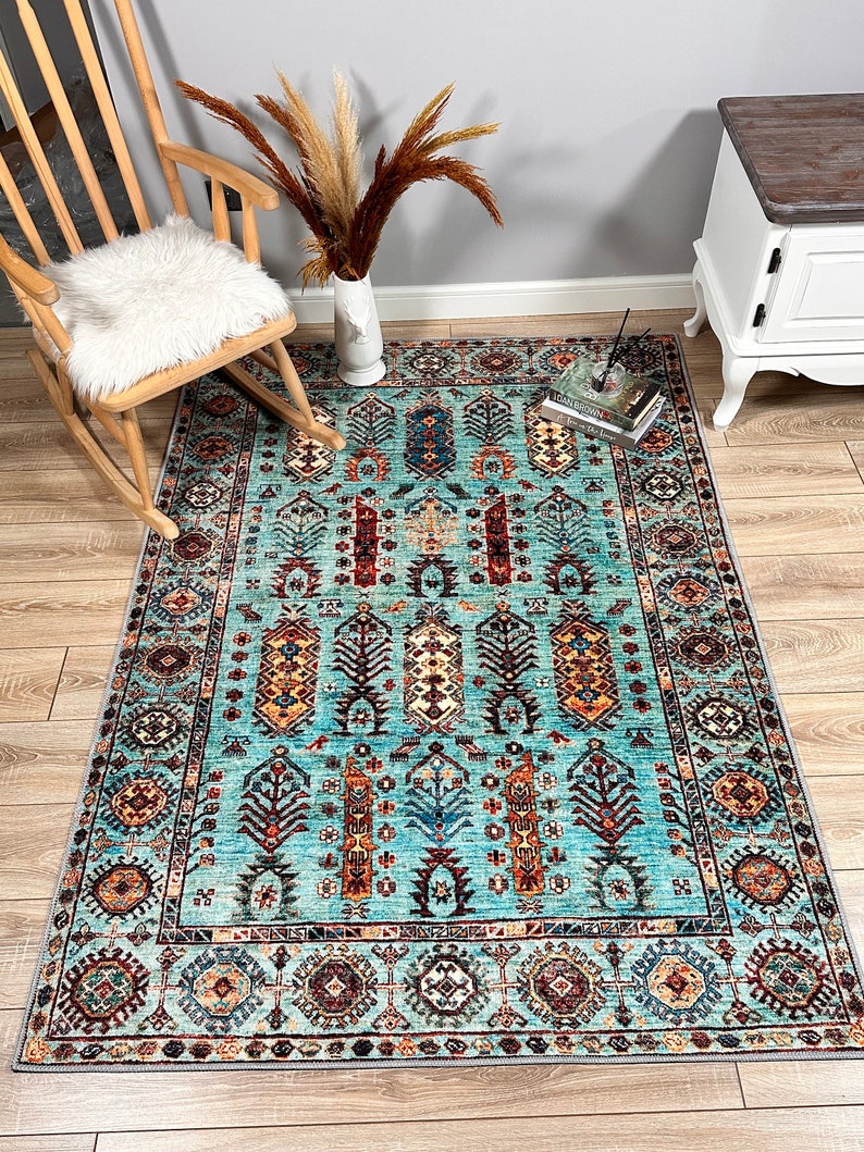 May include: A teal blue rug with a traditional Persian design. The rug features intricate patterns in shades of red, orange, yellow, and brown. The rug is laid out on a wooden floor.