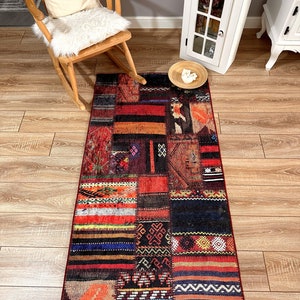 Puede incluir: Una alfombra larga y rectangular de patchwork con una variedad de colores y patrones. La alfombra está hecha de diferentes piezas de tela cosidas juntas, creando un aspecto único y ecléctico. La alfombra es principalmente roja, naranja y negra, con algunos acentos blancos y amarillos.
