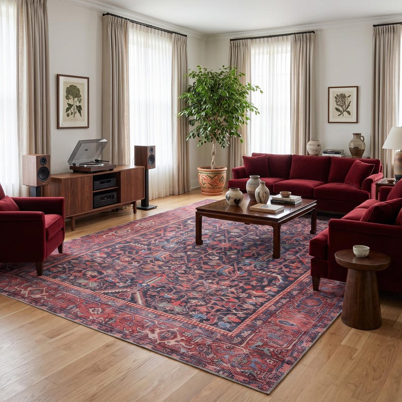 May include: A large rectangular area rug featuring a dark navy blue and deep red intricate floral pattern with a wide decorative border, positioned in a living room with red velvet furniture, a wooden coffee table, and a record player console.