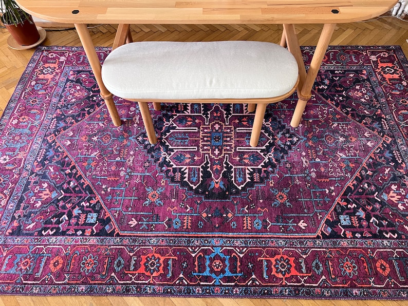 May include: A rectangular area rug with a traditional Persian design in shades of deep purple, black, and teal. The rug is placed under a wooden table and a white bench. The rug's intricate patterns include floral and geometric motifs.