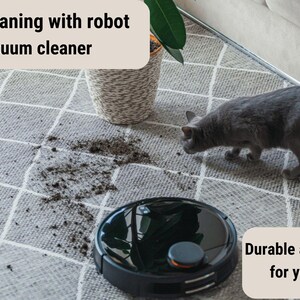 May include: A black robot vacuum cleaner on a gray and white patterned rug with a gray cat and dirt on the rug. The text "Easy cleaning with robot vacuum cleaner" is at the top of the image and the text "Durable and healthy for your pets" is at the bottom of the image.