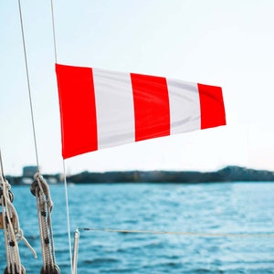 Peut inclure: Un cône de vent rouge et blanc, également appelé girouette, est attaché au mât d'un voilier. Le cône de vent est agité par le vent, indiquant la direction du vent.
